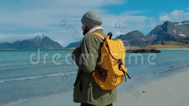 穿着绿色夹克和黄色背包的旅行者<strong>站在海滩上</strong>，<strong>站在</strong>高山峰的背景下